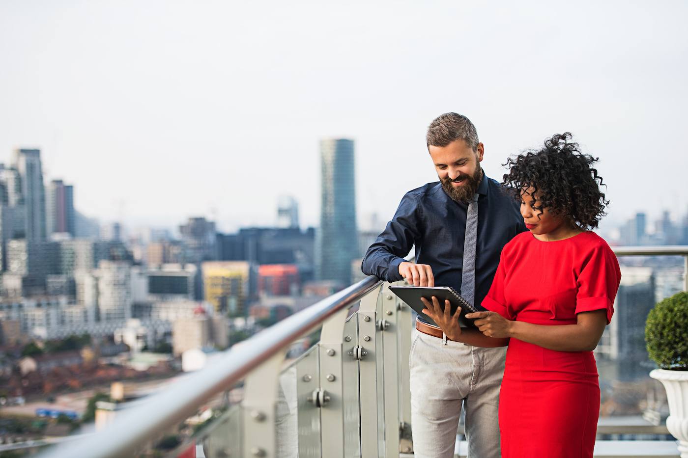 Two business people stood outside on a balcony going over notes with a cityscape in the background